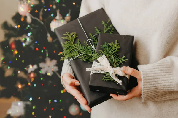 Niña sosteniendo pequeños regalos en sus manos. árbol de Navidad decorado en el fondo —  Fotos de Stock