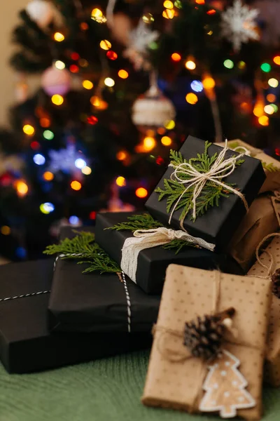 Some gift boxes laying on green textile, defocused light on Christmas tree on background — Stock Photo, Image