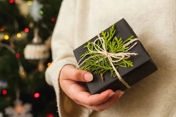 Boîte cadeau confortable dans les mains des femmes. Arbre de Noël décoré sur fond. — Photo