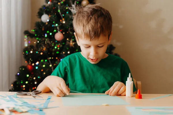 テーブルに座ってクリスマスカードを作る小さな男の子 — ストック写真
