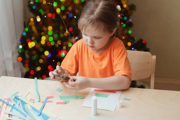 女の子はクリスマスカードをテーブルに座って作る — ストック写真