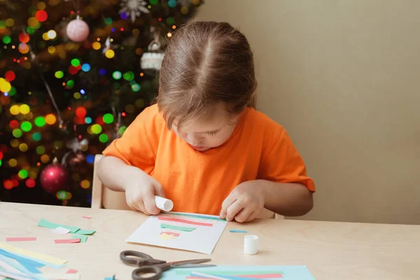 女の子はクリスマスカードをテーブルに座って作る — ストック写真