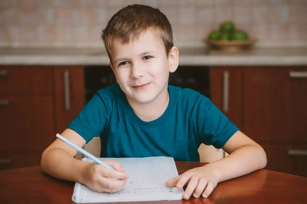 Cute menulis surat anak di notebook duduk dengan meja — Stok Foto