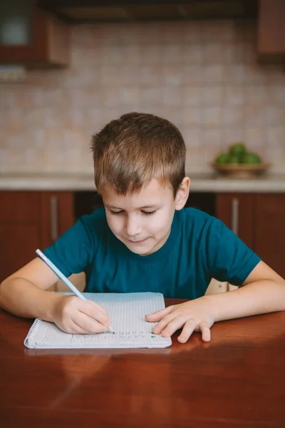 탁자 옆에 앉아서 공책에 글자를 쓰는 귀여운 어린이 — 스톡 사진