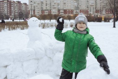 Happy boy standing inside snowcastle and play snowball game in winter park