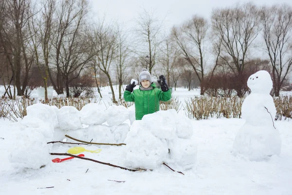 Happy boy standing inside snowcastle and play snowball game in winter park — Stok Foto