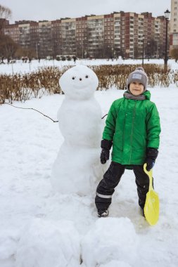 Happy boy standing near snowman in winter park