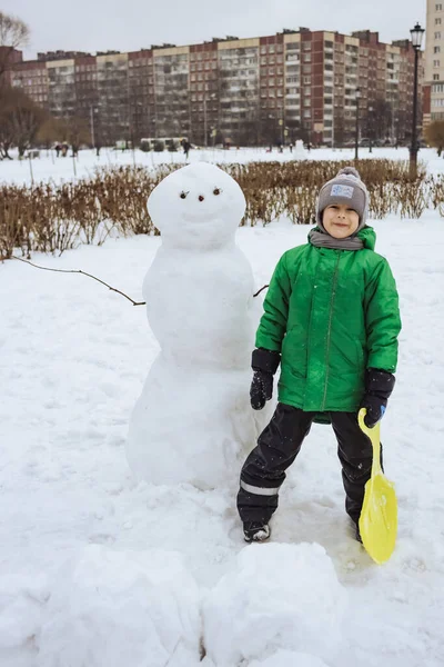 Happy boy standing near snowman in winter park — Stok fotoğraf
