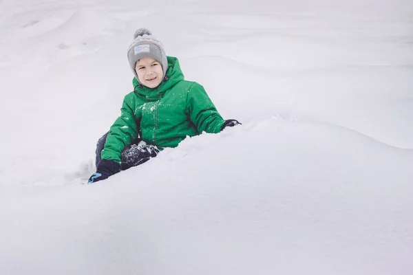 Happy boy duduk di atas salju di taman musim dingin — Stok Foto