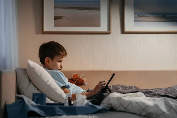 小男孩躺在客厅的床上用平板电脑. — 图库照片