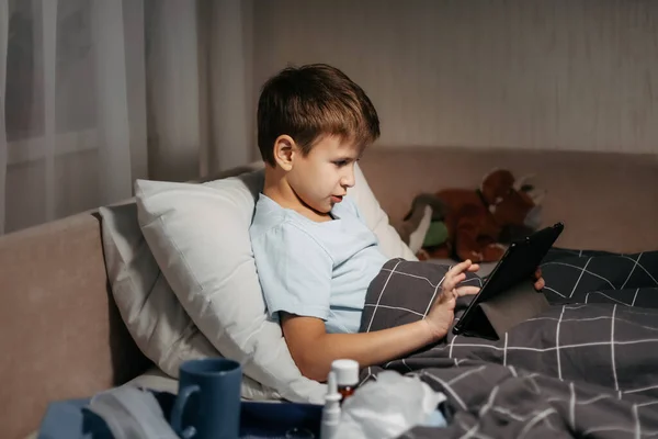 Anak kecil menggunakan tablet saat berbaring di tempat tidur di ruang tamu. — Stok Foto