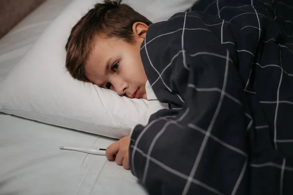 生病的孩子躺在床上，拿着计时器 — 图库照片