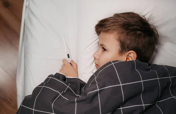 Krankes Kind liegt im Bett und hält Thermometer — Stockfoto