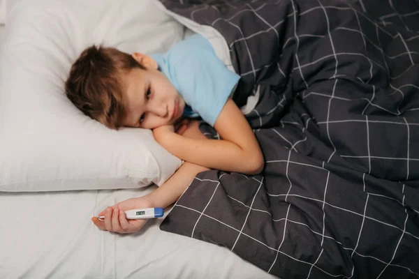 Beteg gyermek feküdt az ágyban, és gazdaság termométer — Stock Fotó
