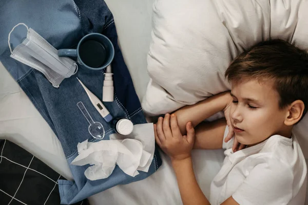 Beteg gyerek fekszik az ágyon. Néhány gyógyszer és hőmérő fekszik a közelben. Kilátás felülről — Stock Fotó
