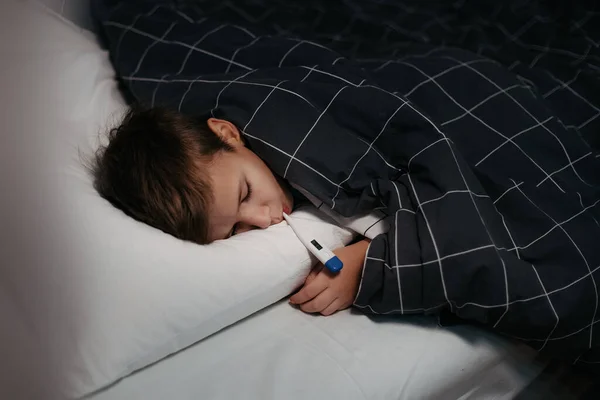 Triste enfant couché au lit avec thermomètre dans la bouche — Photo