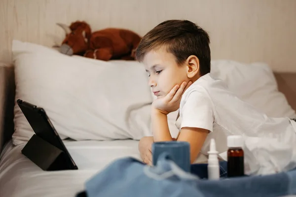 Anak kecil menggunakan tablet saat berbaring di tempat tidur di ruang tamu. — Stok Foto