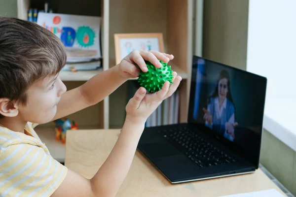 8 tahun anak laki-laki tua duduk dengan meja dengan laptop dan melakukan latihan dengan bola pijat — Stok Foto