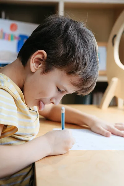 Seorang anak sekolah yang melakukan pelajaran matematika duduk di meja di ruang anak-anak — Stok Foto