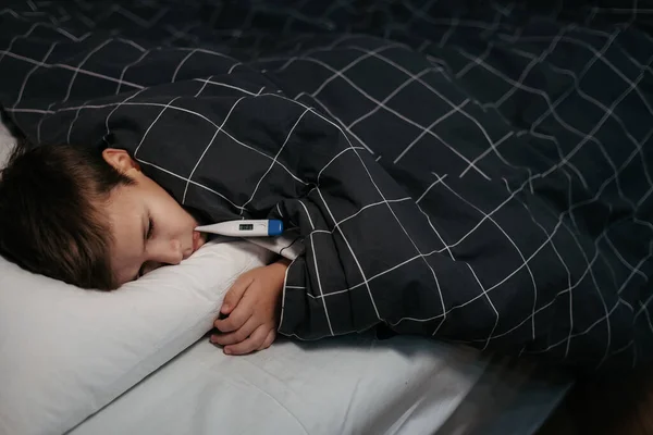 Trauriges Kind liegt mit Thermometer im Mund im Bett — Stockfoto