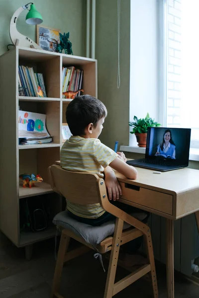 8 tahun anak laki-laki tua duduk dengan meja dengan laptop dan melakukan tugas menulis selama pelajaran online — Stok Foto