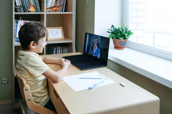 8 살 소년은 책상 옆에 노트북을 놓고 앉아서 온라인 수업중에 과제를 작성 합니다. — 스톡 사진