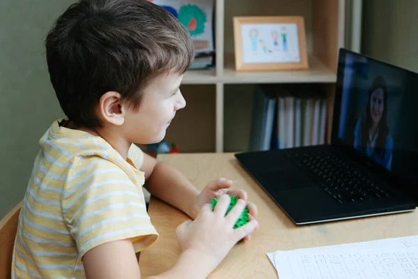 8岁的男孩带着笔记本电脑坐在办公桌旁，用按摩球做运动 — 图库照片