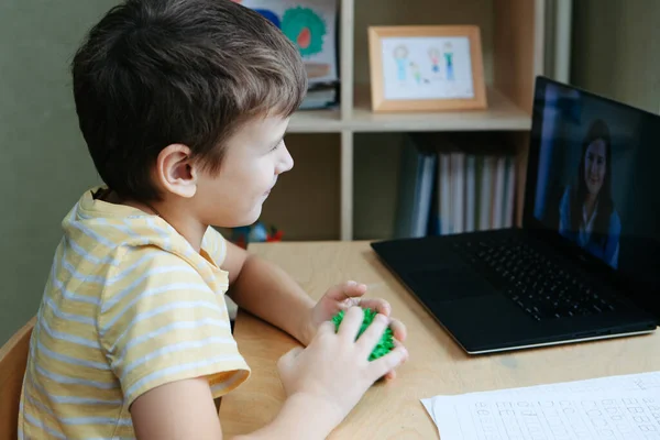 8 ans garçon assis par bureau avec ordinateur portable et faire de l'exercice avec boule de massage Images De Stock Libres De Droits