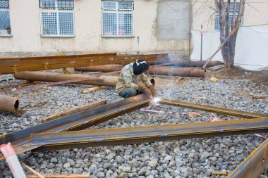 Koruyucu maskeli kaynakçı açık havada metal kaynak yapıyor..
