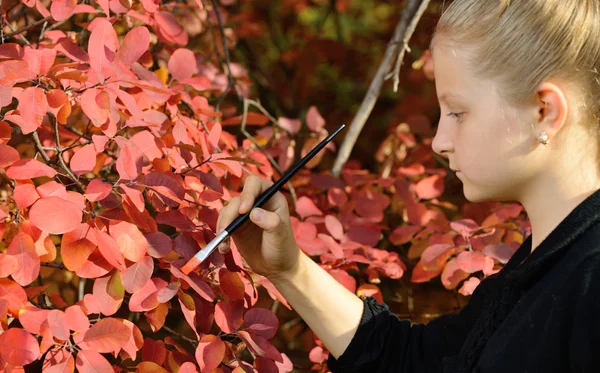 Pintura menina na cor vermelha da folhagem das árvores — Fotografia de Stock