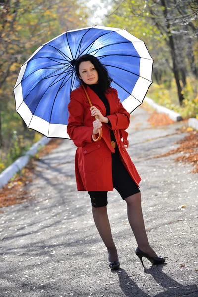 Schöne Frau in rotem Mantel und mit blauem Regenschirm — Stockfoto