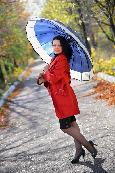 Mooie vrouw in een rode mantel en met een blauw paraplu — Stockfoto