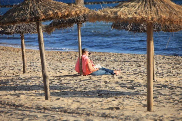 Person reading under a thatched beach umbrella — Stock Photo, Image