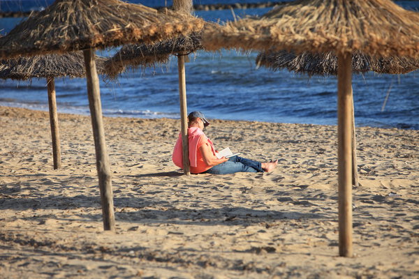 Person reading under a thatched beach umbrella