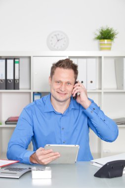 holding bir telefon ve bir tablet bilgisayar masasında çalışan iş adamı