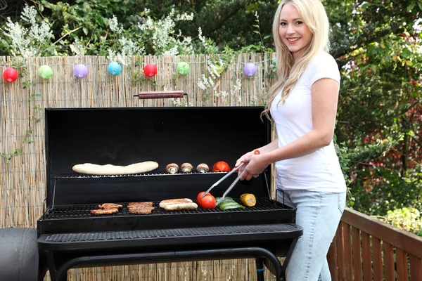 Mooie blonde vrouw barbecueën op een patio — Stockfoto