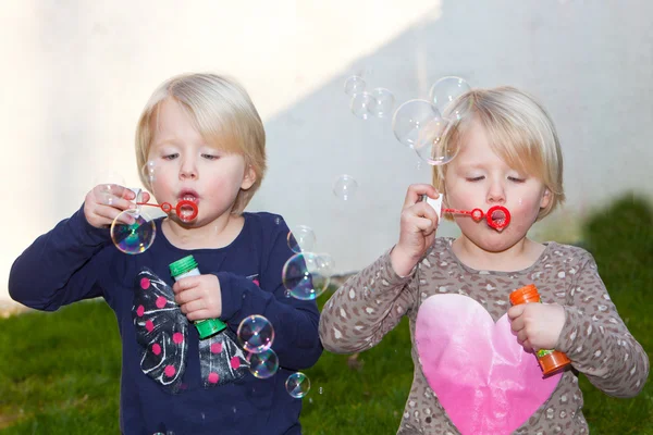 Two beautiful blond twins blowing bubbles — Stock Photo, Image