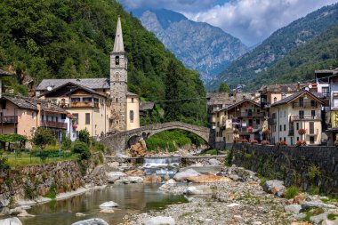 İtalya 'nın Aosta Vadisi' ndeki Fontainemore kasabasındaki evler, eski kilise ve ortaçağ taş köprüsü boyunca uzanan dağ nehri..