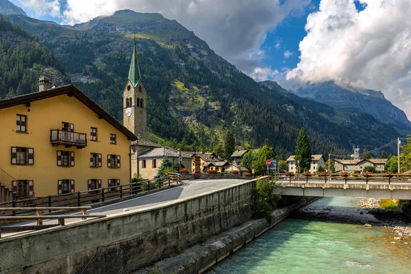 イタリアのAosta ValleyのGressoney Saint Jeanの小さな町を背景に 家や古い教会に沿って山の川に架かる橋 — ストック写真