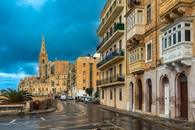 Malta Valletta 'da tipik bir meskun bina ve güzel bulutlu gökyüzünün altındaki ıslak şehir caddesi..