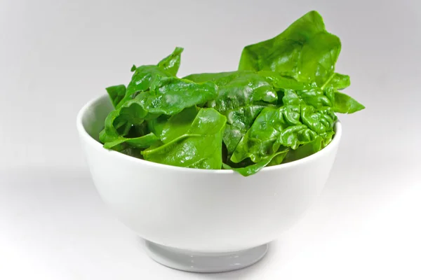 Beyaz arka plan beyaz bir kase Çiğ ıspanak yaprakları