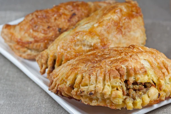 pasties filled with minced meat on a white plate with beige background