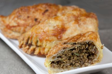 pasties filled with minced meat on a white plate with beige background