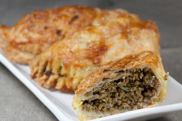 Pastéis cheios de carne picada em uma placa branca com fundo bege — Fotografia de Stock