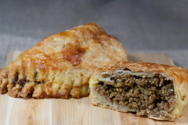 bej renkli arka plan ile ahşap bir tahtada kıyma ile dolu pasties