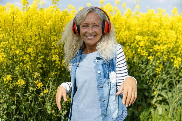 Пожилая Женщина Слушает Музыку Наушниках Цветущем Поле Канолы — стоковое фото