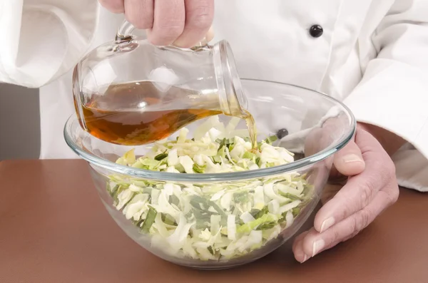 Female chef fills some oil into a salad — Stock Photo, Image