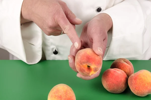 Female chef shows with her index finger on a peach — Stock Photo, Image