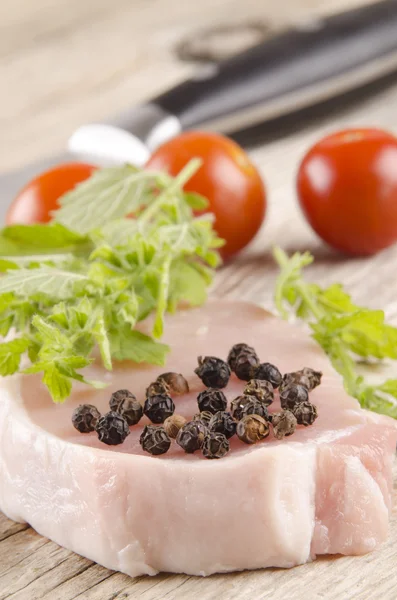 Pork chop and peppercorns on a wooden table — Stock Photo, Image