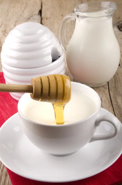 Honey flows into a cup with warm milk — Stock Photo, Image